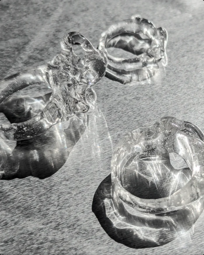Clear hand-formed resin rings catching sunlight on brushed metal